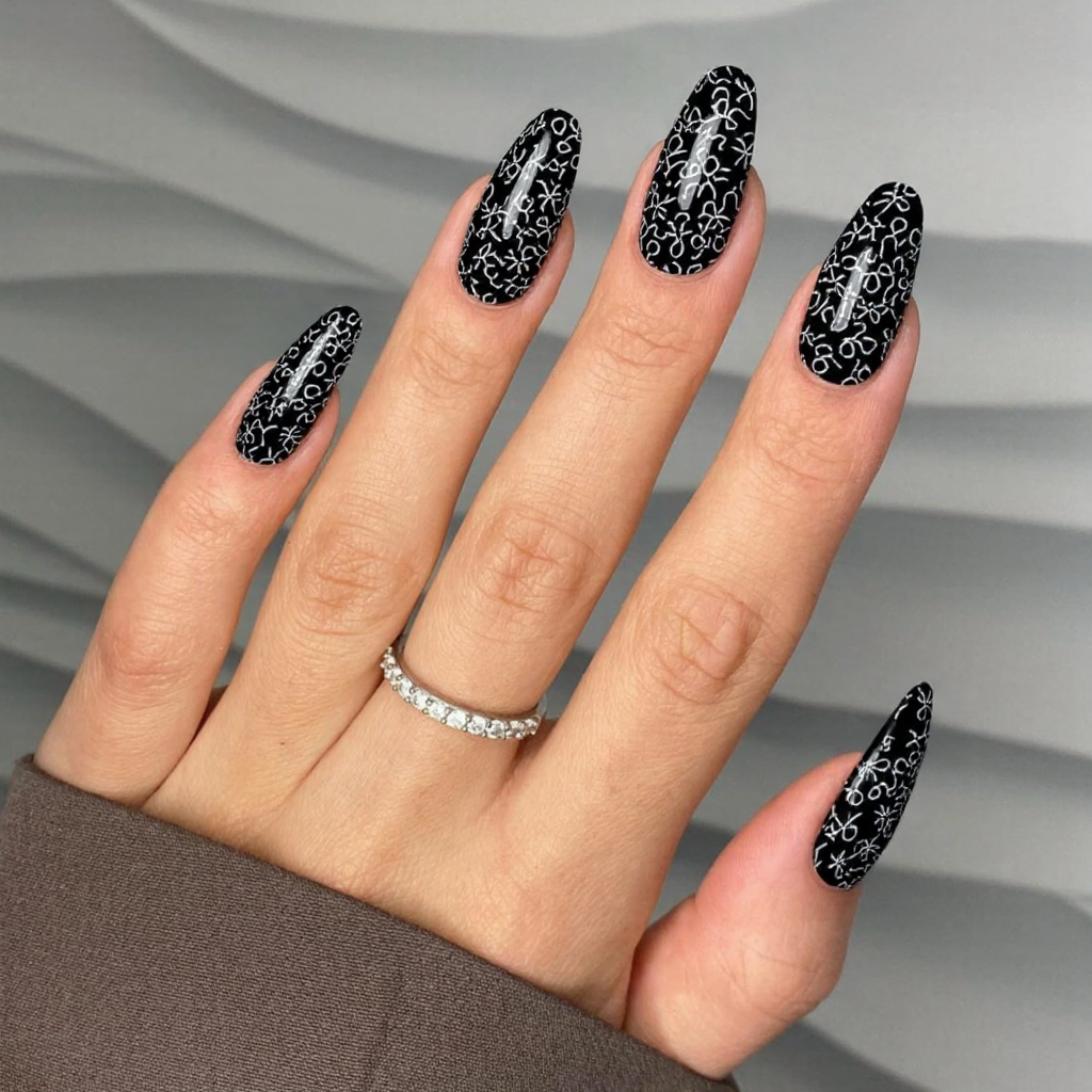 Long almond nails in black with delicate white floral outlines for a chic monochrome vibe.