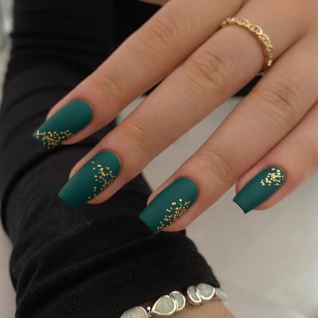 Short stiletto nails in matte emerald green with tiny gold leaf decals for a sophisticated autumn look.