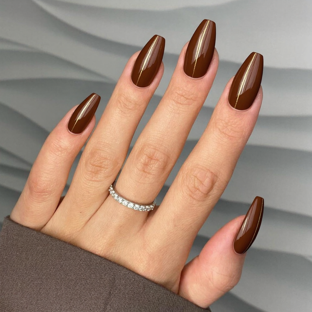 Long almond nails in a chocolate-brown with subtle gold striping for a luxurious vibe.
