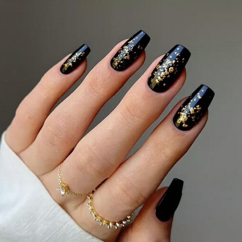 Medium stiletto nails in black with a few gold foil flakes on each nail for an edgy glam look.