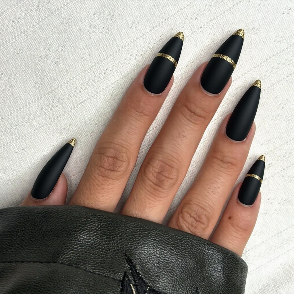 Long stiletto nails in matte black, each topped with a thin line of gold glitter near the tips.