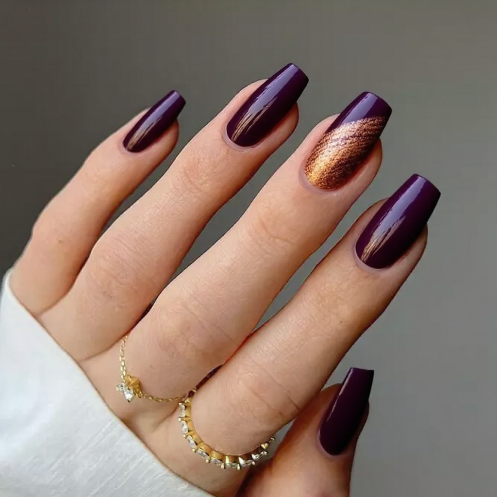Medium stiletto nails in deep plum with a subtle copper foil swirl on the ring finger.
