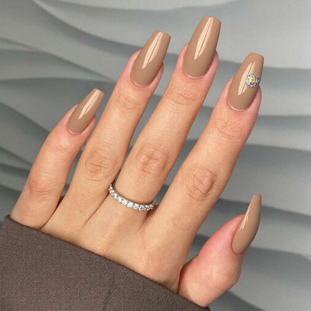 Long almond nails in a nude base with a gold foil accent near the cuticles, spotlighting the engagement ring.