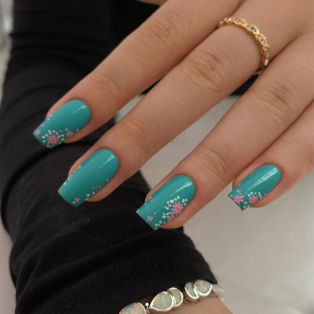 Short stiletto nails in a glossy teal with tiny cartoon flowers near the tips for a cute, cheerful look.