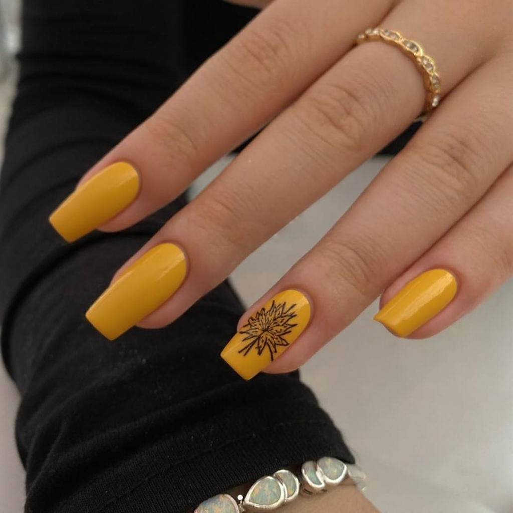 Short stiletto nails in mustard yellow with one accent nail featuring a hand-painted autumn leaf.