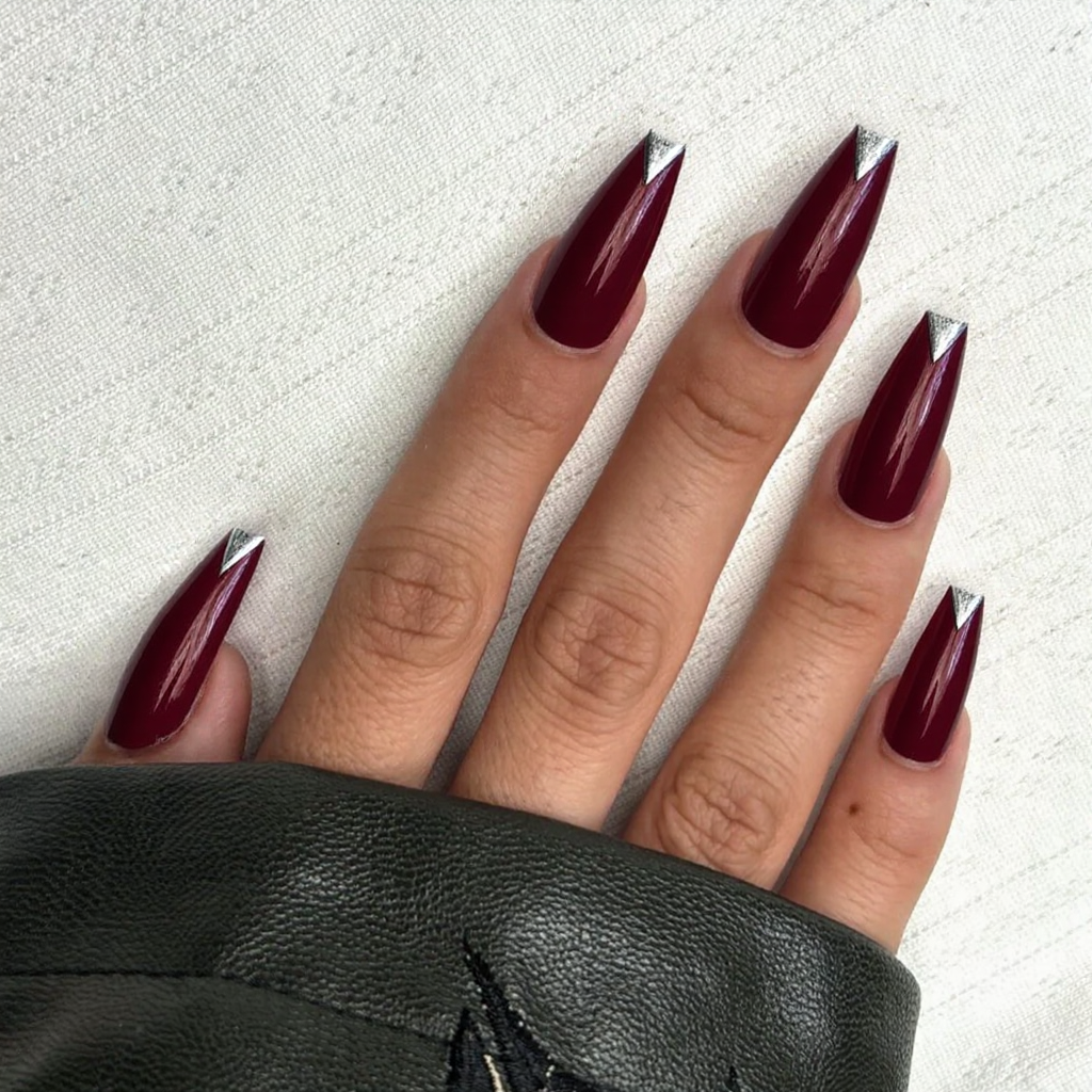 Long stiletto nails in a deep scarlet, each with a V-shaped silver French tip for added drama.