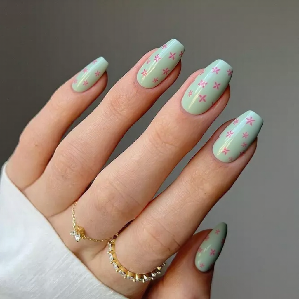 Medium stiletto nails with a pale green base and tiny pink flower decals for a fresh, floral touch.