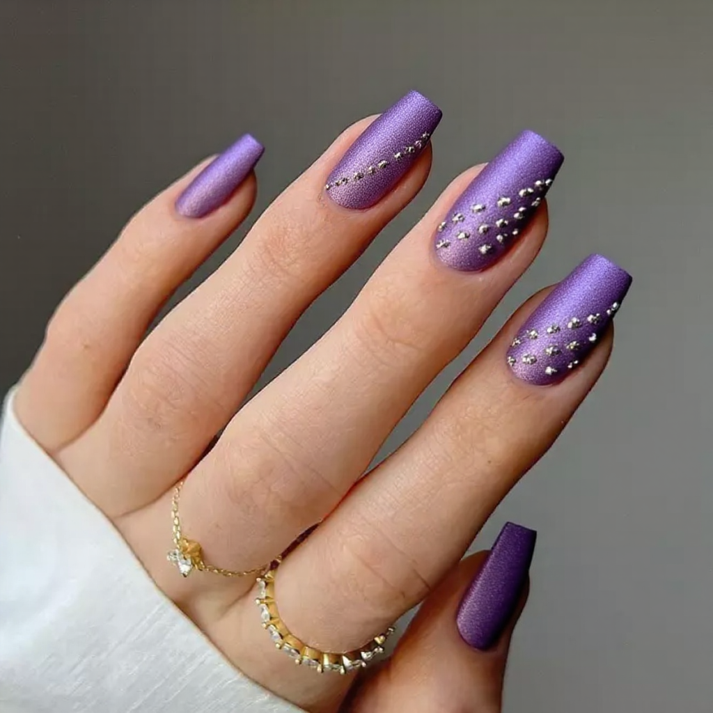 Medium stiletto nails in a metallic violet with a diagonal line of silver studs on each accent nail.