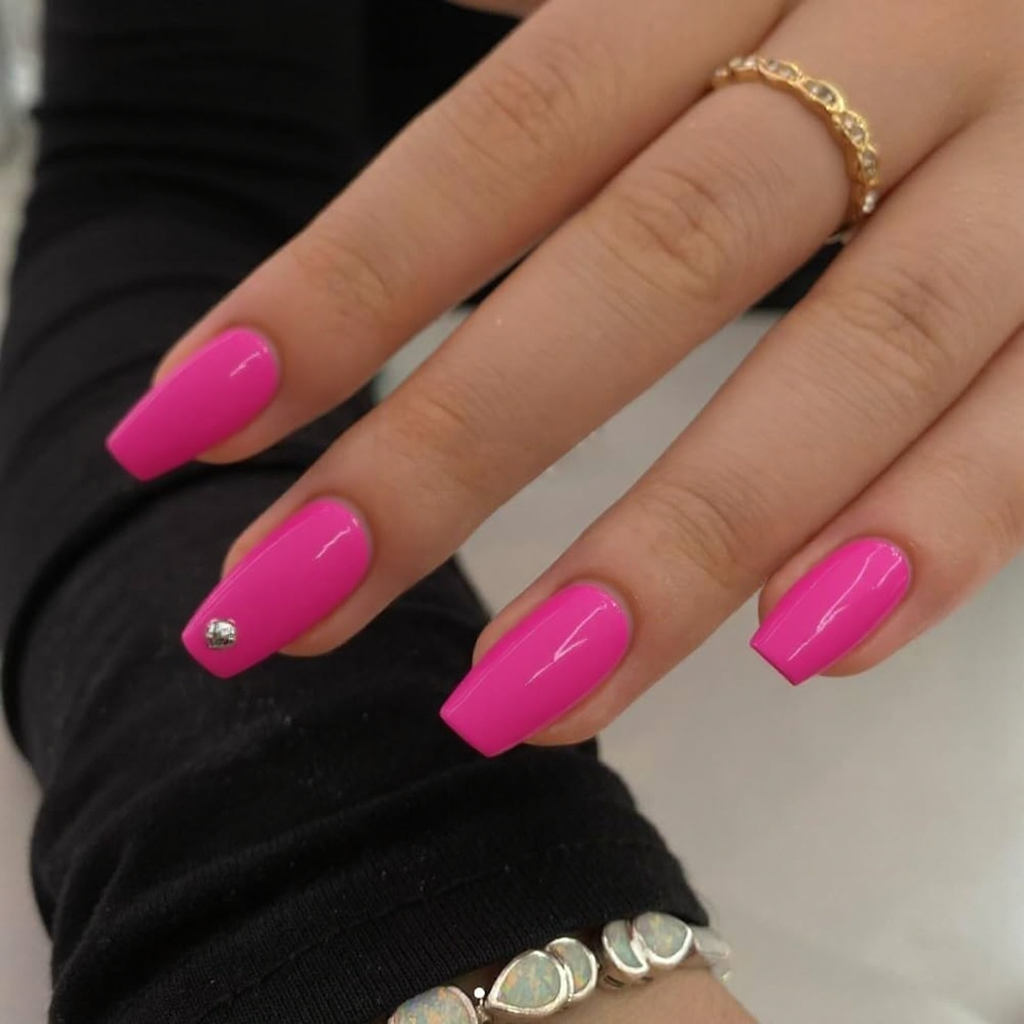 Short stiletto nails in hot pink, each featuring a tiny silver stud near the tip for a fun detail.