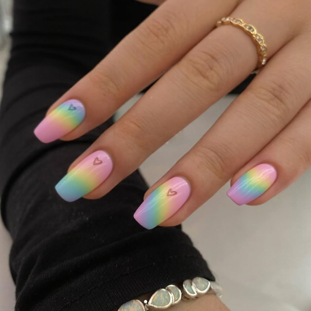 Short stiletto nails in a pastel rainbow gradient with a small heart shape cutout on each ring finger.