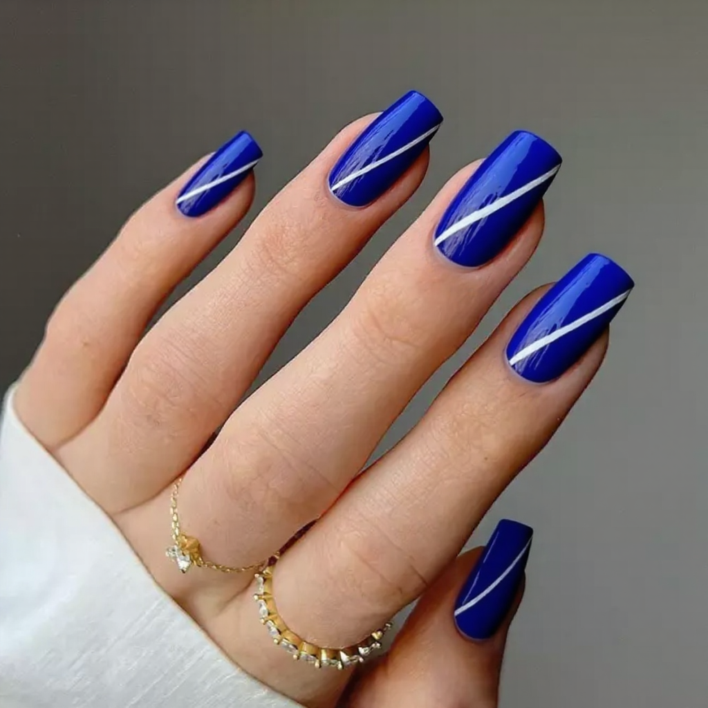 Medium stiletto nails in a cobalt blue, each with a thin diagonal white stripe for contrast.
