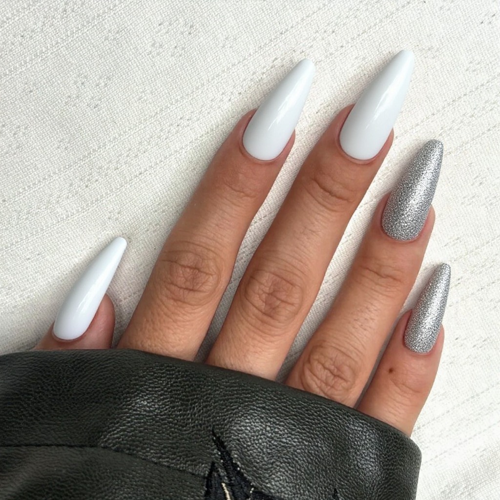 Long stiletto nails in white with a fine silver glitter fade on the ring finger, ideal for an engagement reveal.