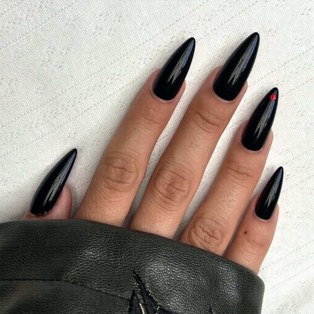 Long stiletto nails in a glossy black, each adorned with a tiny red gem near the tip for drama.