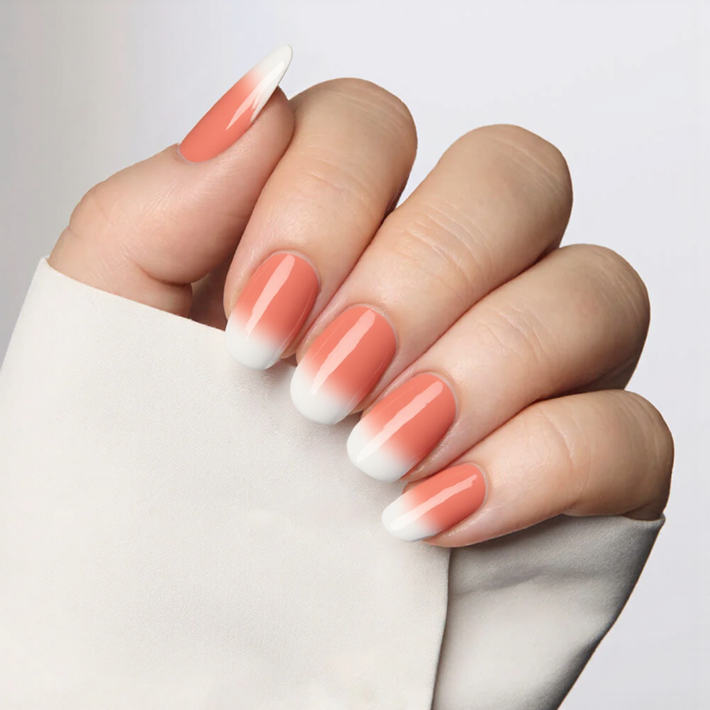 Medium almond nails in a coral shade with a faint ombre effect transitioning to white tips for a graceful style.