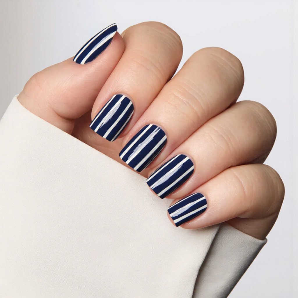 Short square nails in a navy blue with white stripes, inspired by nautical themes for a summer trip.