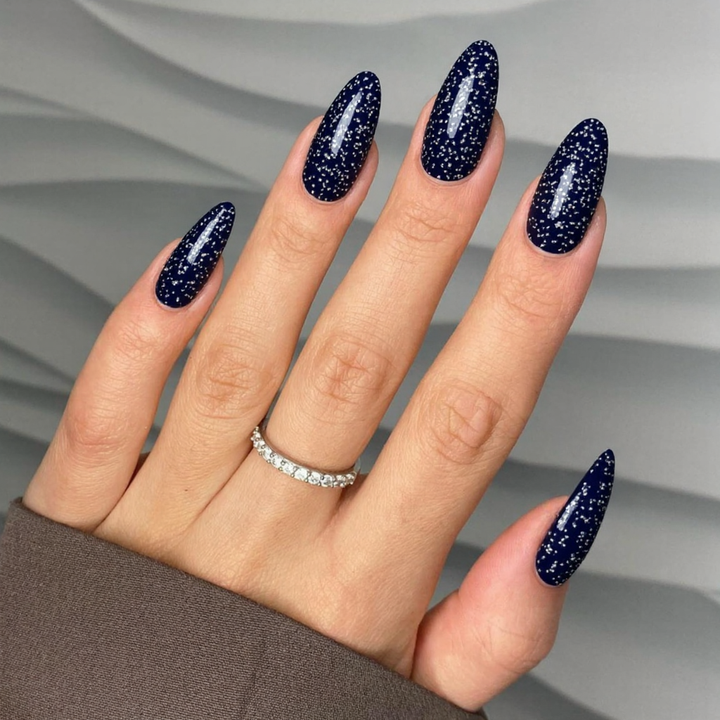 Long almond nails in a deep navy blue with silver geometric patterns for a modern holiday look.