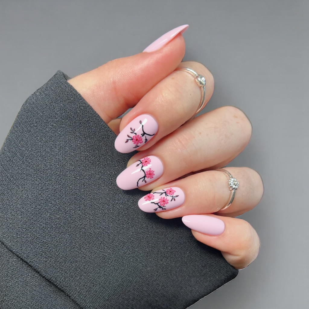 Short almond nails with a delicate Japanese cherry blossom nail art motif on a soft pink background.