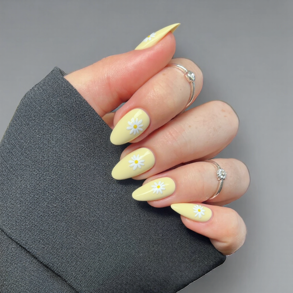 Short almond nails in a pastel yellow, each with a small white daisy design for a cheerful vibe.