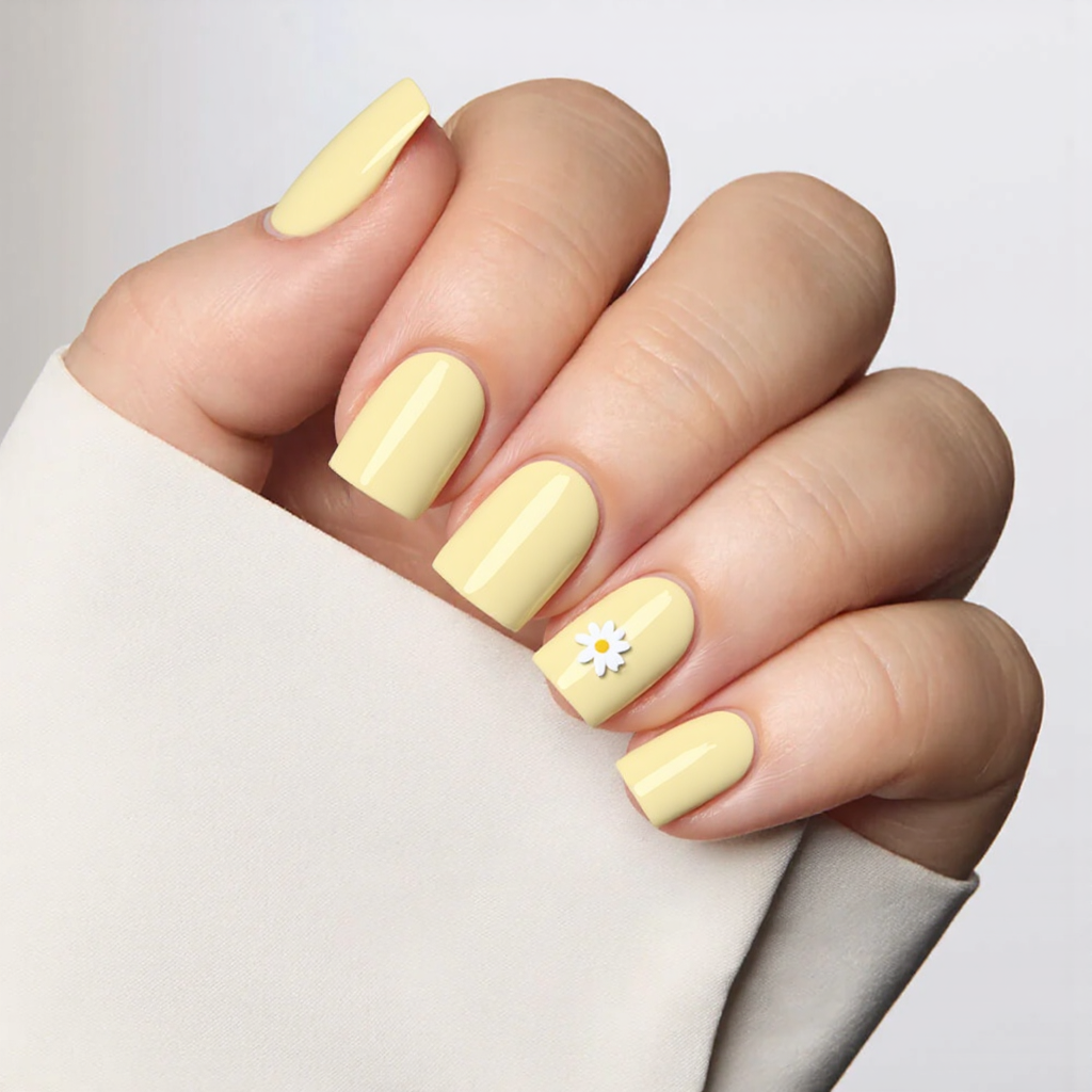 Short square nails in pastel yellow with a tiny white daisy on the ring finger for a cute accent.