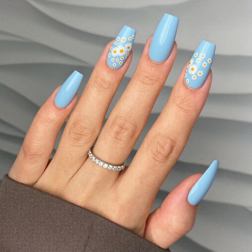 Long almond nails in a soft sky-blue with a few daisies drawn on the ring finger for a sweet spring accent.