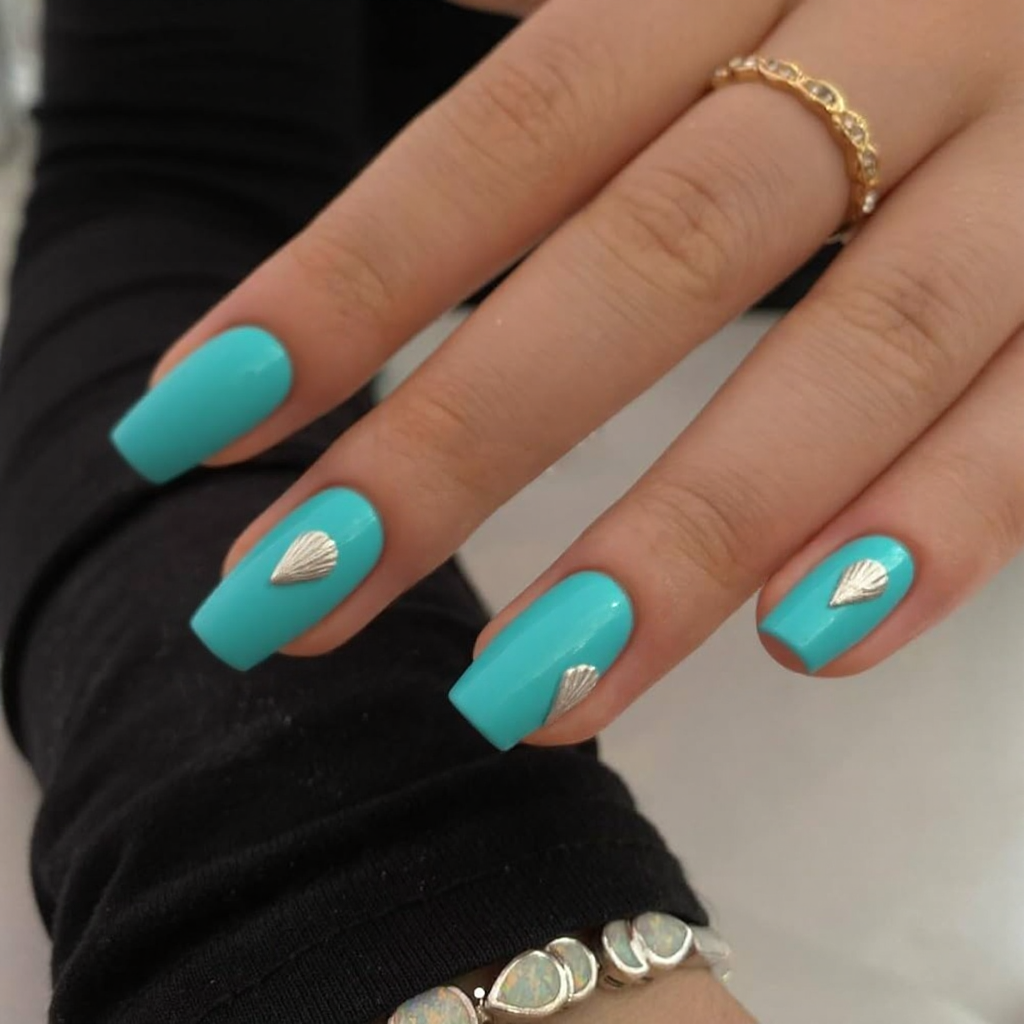 Short stiletto nails in a bright aqua shade, each with a mini seashell decal for a beachy vibe.