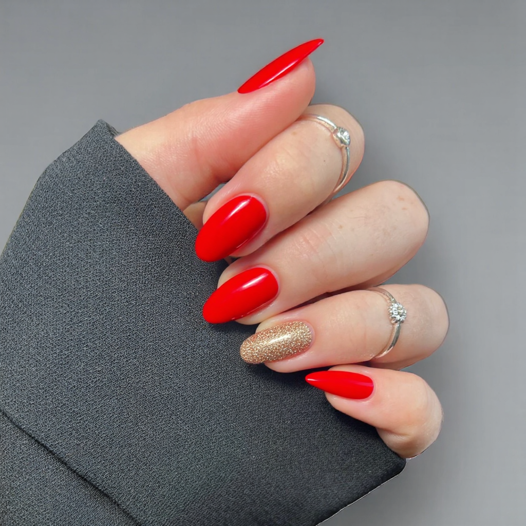 Short almond nails in a festive red with subtle gold glitter accents for a Christmas-inspired look.