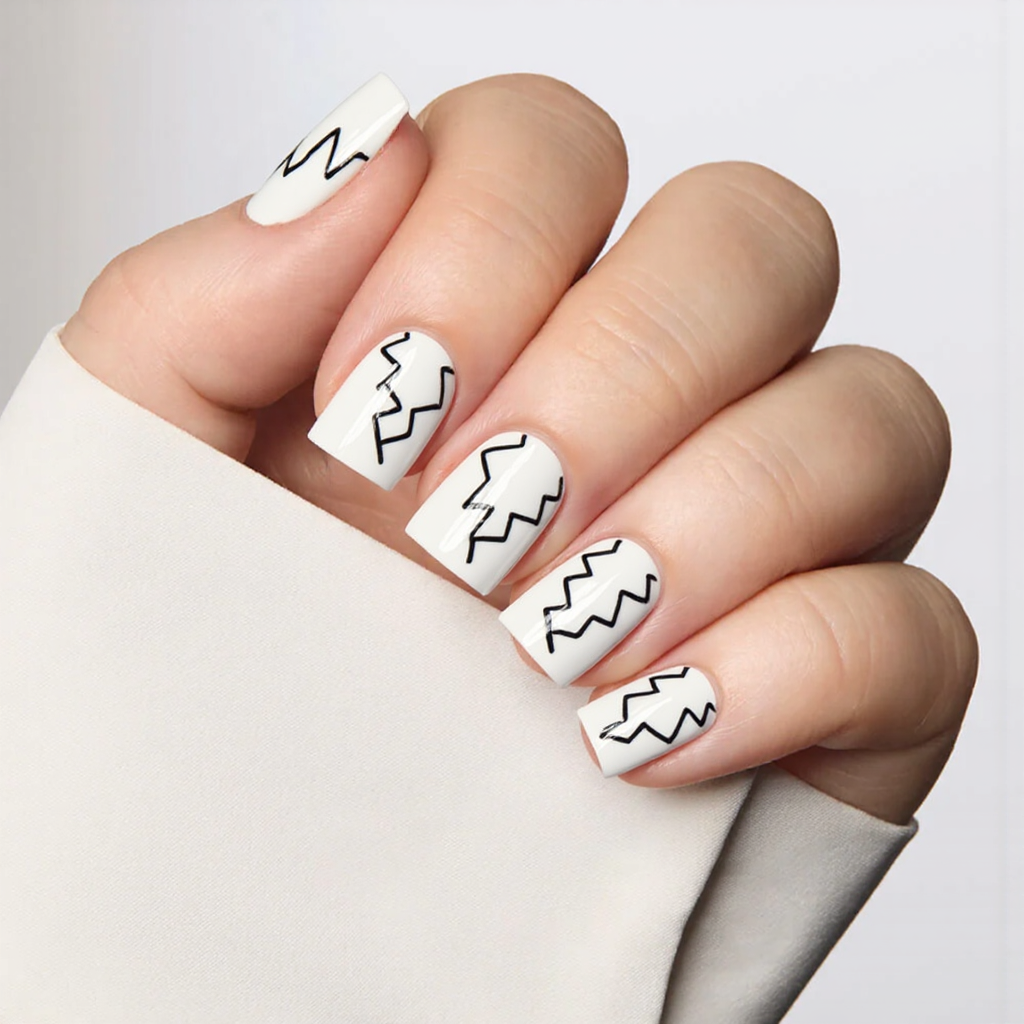 Short square nails in bright white, each with a thin black zigzag pattern for a fun contrast.