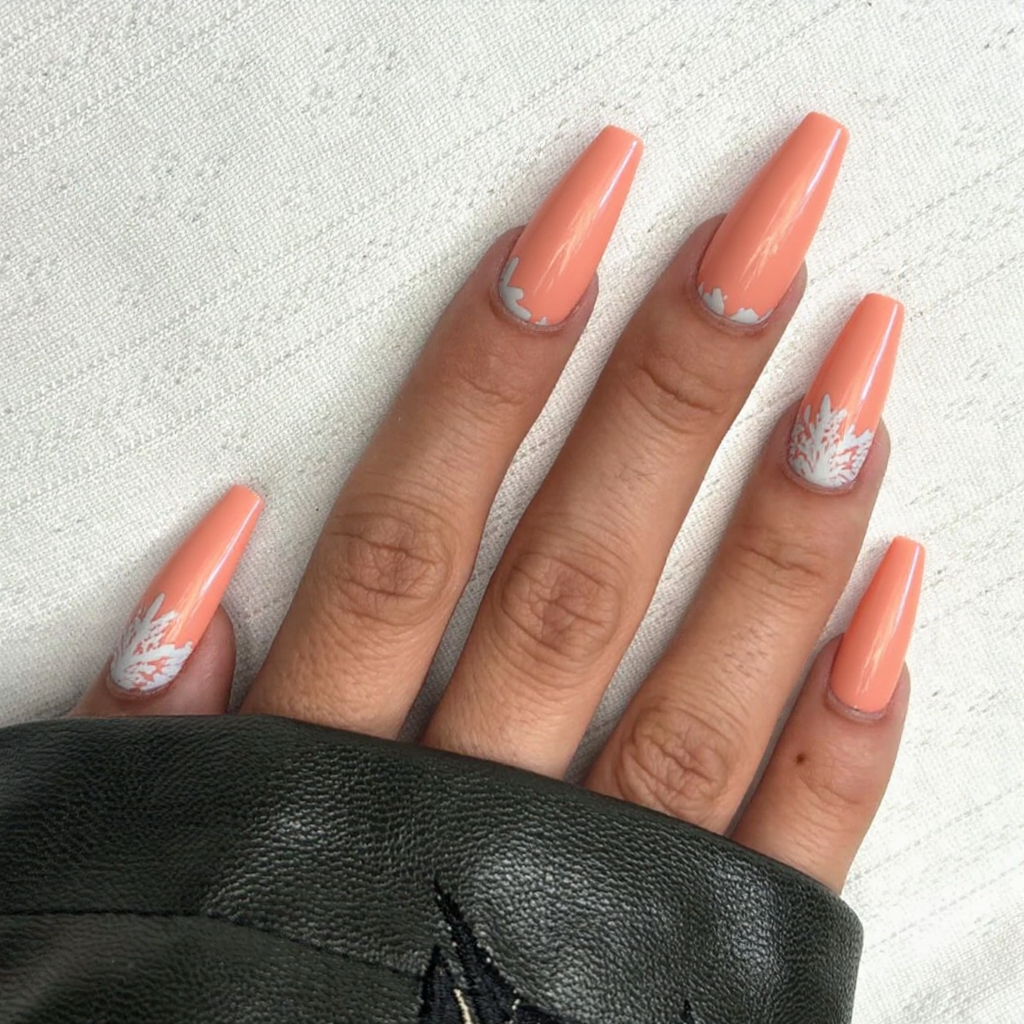 Long stiletto nails in a soft coral, each featuring a delicate white seashell pattern at the tips.