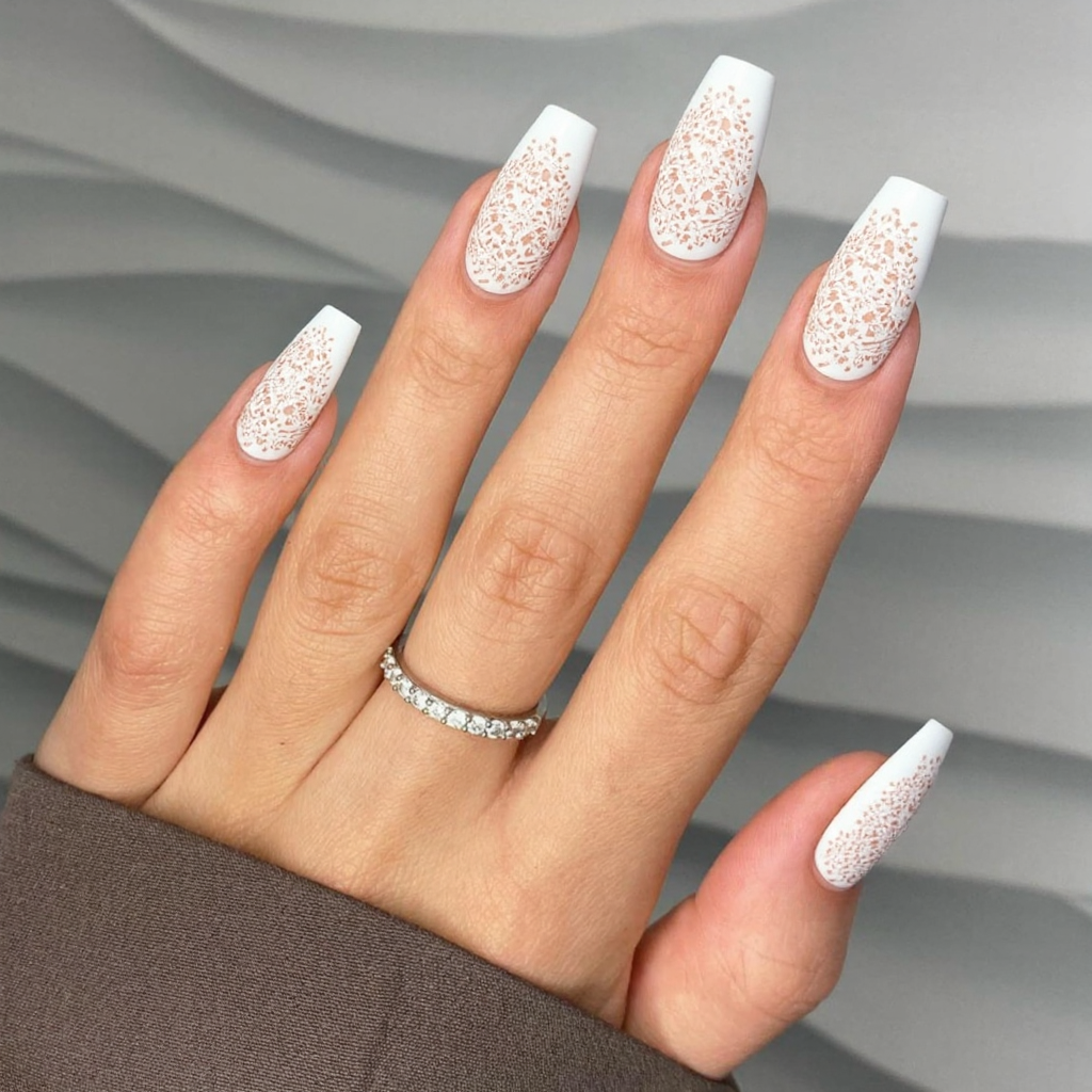 Long almond nails in a pure white, with a delicate, hand-painted lace design on the ring fingers.