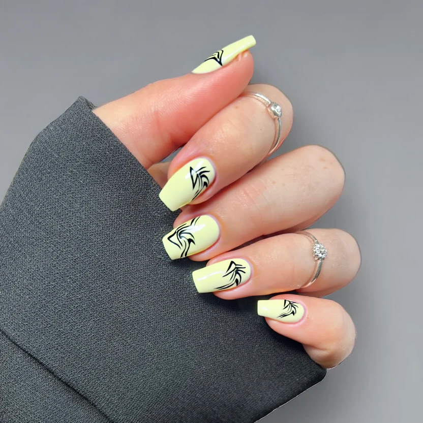 Nails featuring a soft pastel yellow base, complemented by intricate minimalist black Griffin motifs delicately hand-painted on the ring fingers. The design showcases just a few elegant lines to represent the mythical creature, adding a touch of sophistication while keeping the overall look refined. The remaining nails are painted in a uniform pastel yellow, providing a harmonious and balanced appearance. A glossy finish enhances the nails’ vibrant colors, perfectly suited to the gentle curves of short almond-shaped nails.