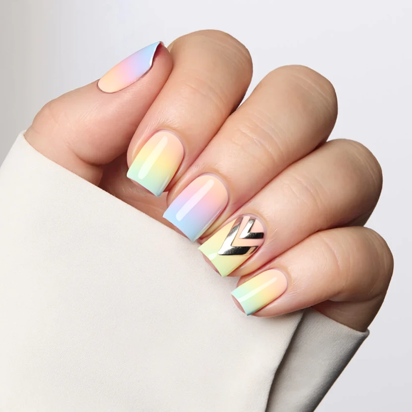 Nails painted in a soft gradient reminiscent of a colorful sunset, transitioning smoothly from pastel pink at the base through delicate peach, lavender, and soft blue, culminating in a gentle buttery yellow at the tips. This elegant design maintains a minimalist approach, with only the ring and middle fingers adorned with tasteful, abstract lines in a subtle metallic silver, placed delicately along the edges to enhance the modern feel. The remaining nails showcase the same smooth gradient as a cohesive background, finished with a glossy topcoat to ensure brightness and a fresh, polished look, perfectly complementing the square shape and short size of the nails.