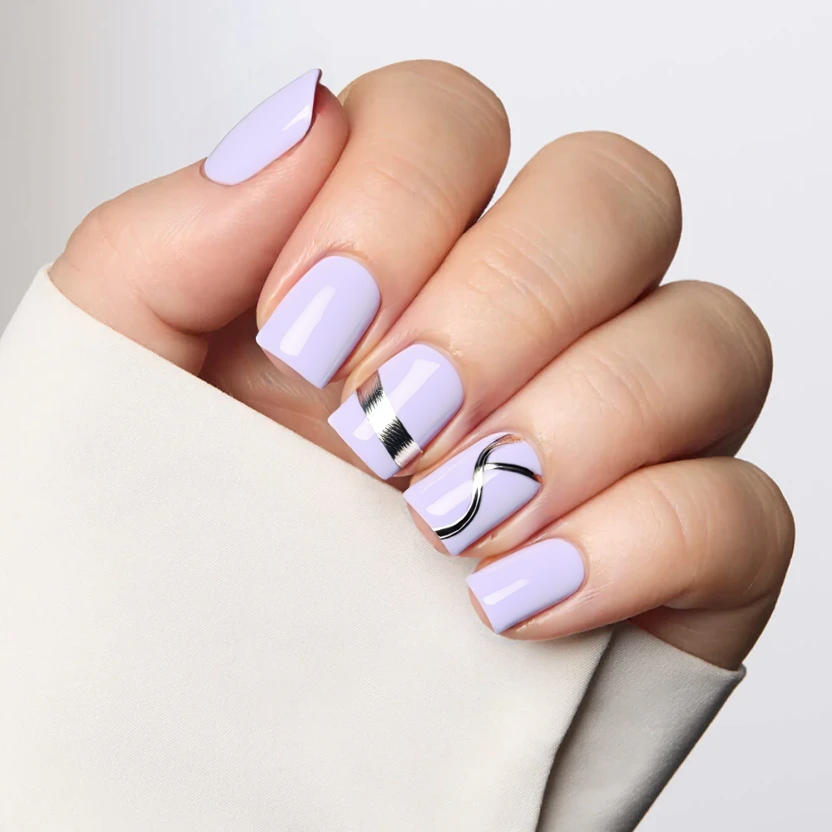 Elegant square nails featuring a soft lavender base color that provides a delicate and feminine touch. On the thumb and ring finger, minimalistic silver foil accents create a sleek design, with the foil art arranged in simple, curved lines that flow gently across the nails. The rest of the nails remain polished in solid lavender, offering a harmonious balance between bold yet understated aesthetics. A glossy finish enhances the overall look, allowing the silver accents to subtly catch the light while coordinating beautifully with the short square shape.