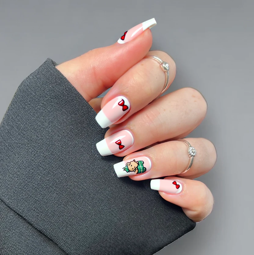 Nails designed for an elegant Christmas party theme, featuring a classic French tip in soft white, contrasted against a delicate pastel pink base. The French tips are highlighted with a soft plaid pattern, incorporating shades of red and green for a seasonal touch on a single ring finger. Each of the remaining nails showcases minimalistic designs: one adorned with a tiny, hand-painted teddy bear in neutral tones placed near the cuticle, while others feature petite bows delicately placed at the tips, crafted in muted tones of red to match the sweater and skirt. The overall look is refined and festive, ideal for short almond-shaped nails, ensuring a chic and coordinated aesthetic without any glittery polish.
