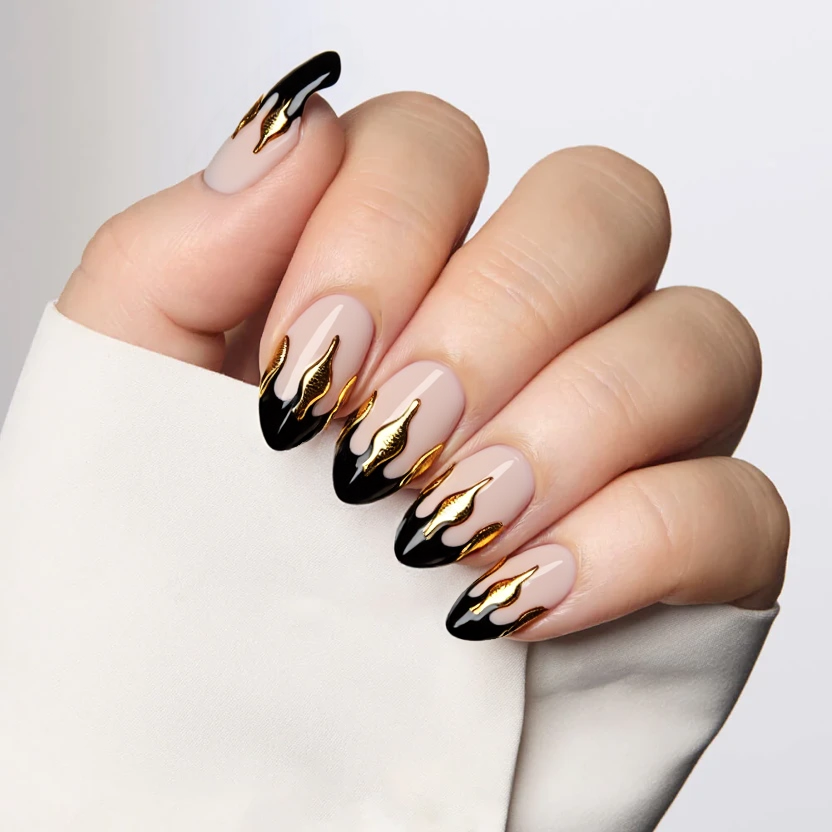 Nails featuring a sheer nude base, providing a soft yet elegant foundation. The almond shape is accentuated by sharp black French tips that add a touch of sophistication. On the ring fingers, delicate gold foil accents shaped like flickering flames are applied, creating a striking contrast against the understated base. The overall design is chic and refined, perfectly balanced for the medium length, with the glossy finish enhancing the luxurious feel of the gold accents.