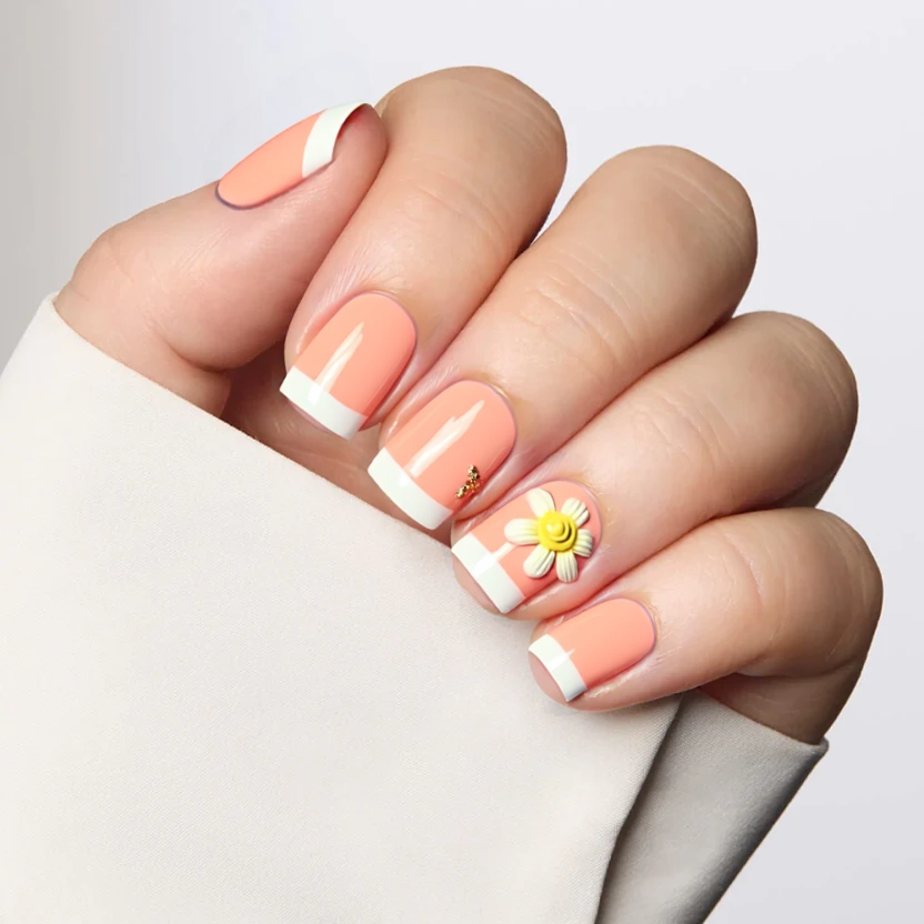Nails coated in a soft pastel orange hue, providing a warm and cheerful base color. One accent nail features a delicate French tip design, incorporating a subtle white line along the edge to create an elegant effect. Adorning this particular nail is a charming yellow flower at the base of the French tip, adding a touch of femininity without overwhelming the design. The remaining nails maintain the smooth orange finish, ensuring a harmonious and balanced look that complements the clean lines of short square nails.