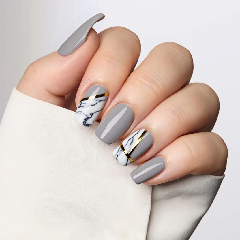 Nails designed in a soft, muted gray base color, allowing for an elegant and modern aesthetic. Two accent nails feature a minimalist marble effect in subtle shades of white and gray, delicately mixed to create a sophisticated look. To enhance the design, thin strips of gold foil are carefully placed along the edges of the marble nails, adding a touch of luxurious shine without overwhelming the overall simplicity. The remaining nails maintain the same muted gray base for a cohesive appearance. Finished with a glossy topcoat, this design perfectly balances modern edge with refined elegance, suitable for medium-length almond-shaped nails.