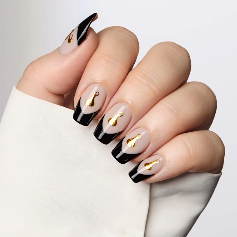 Nails feature a delicate nude base with a sheer finish, beautifully complementing the elegant almond shape. Each nail has a sharp black French tip that adds a striking contrast while maintaining a polished look. On the ring fingers, minimalistic gold foil accents depict tiny flame or drip designs, providing a touch of sophistication and a hint of drama without overwhelming the simplicity. The overall design is sleek and chic, suitable for medium-sized almond nails, finished with a glossy topcoat to enhance the light-catching qualities of the gold foil and ensure a sophisticated shine.