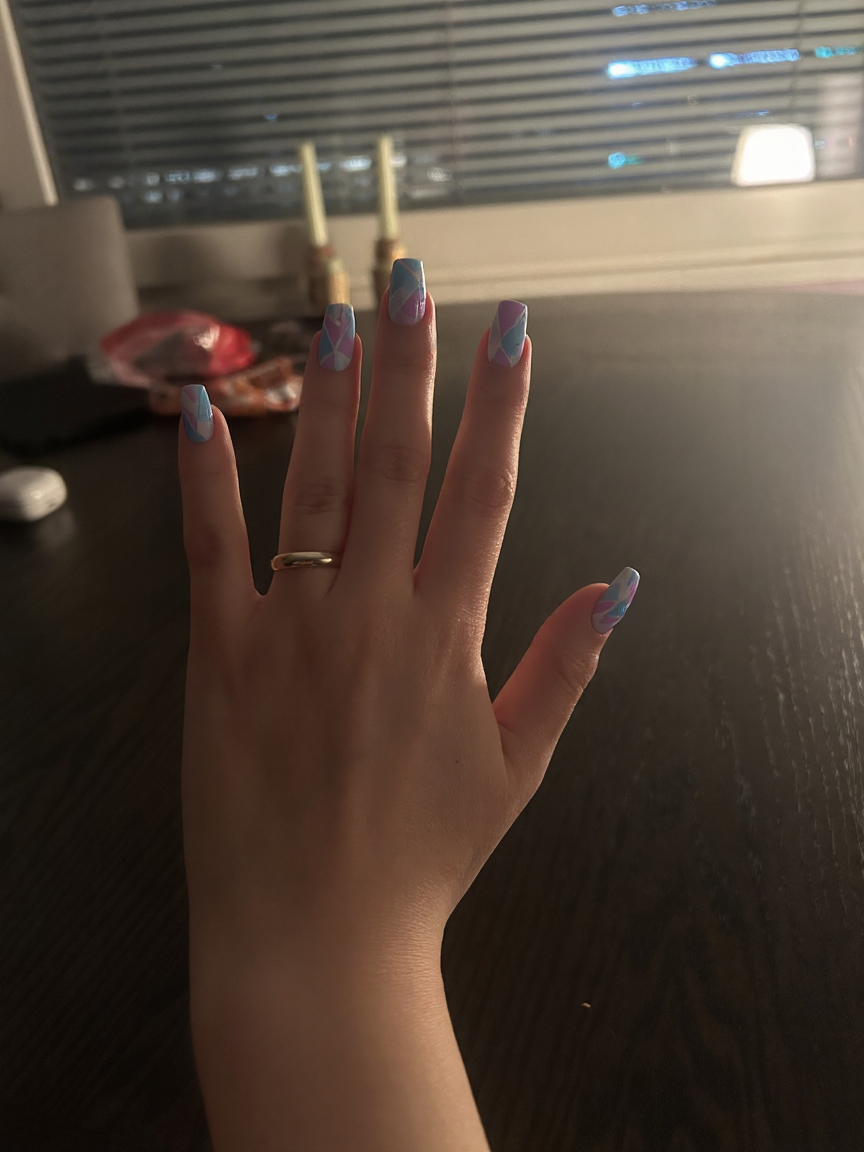 Create a stunning nail art design that features a playful combination of pastel colors in a stiletto shape. Incorporate light blues, soft pinks, and delicate lilacs into a variety of geometric patterns, including sharp triangles, elegant lines, and intriguing shapes that flow seamlessly across the nails. Add a glossy finish to enhance the vibrancy of the colors and consider mixing in some subtle white accents or negative space to create contrast. This design should embody a modern and chic aesthetic, perfect for showcasing a unique style with a light and airy feel.