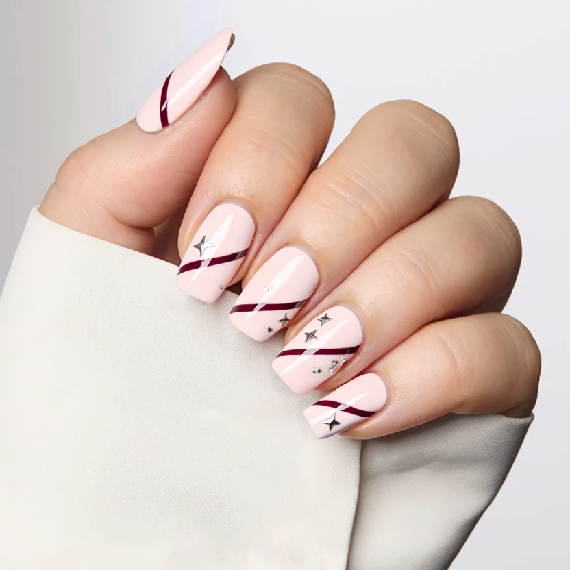 Elegant almond-shaped nails feature a soft pastel pink as the base color, providing a delicate backdrop. On the ring fingers, a playful yet minimal design showcases subtle maroon stripes that run diagonally across the nail, accompanied by evenly spaced silver stars that add a touch of sparkle. The remaining nails maintain the pristine pink base, ensuring a cohesive look while allowing the accented nails to stand out. The overall finish is glossy, enhancing the feminine and whimsical feel of the design, perfectly suited for medium-length nails.