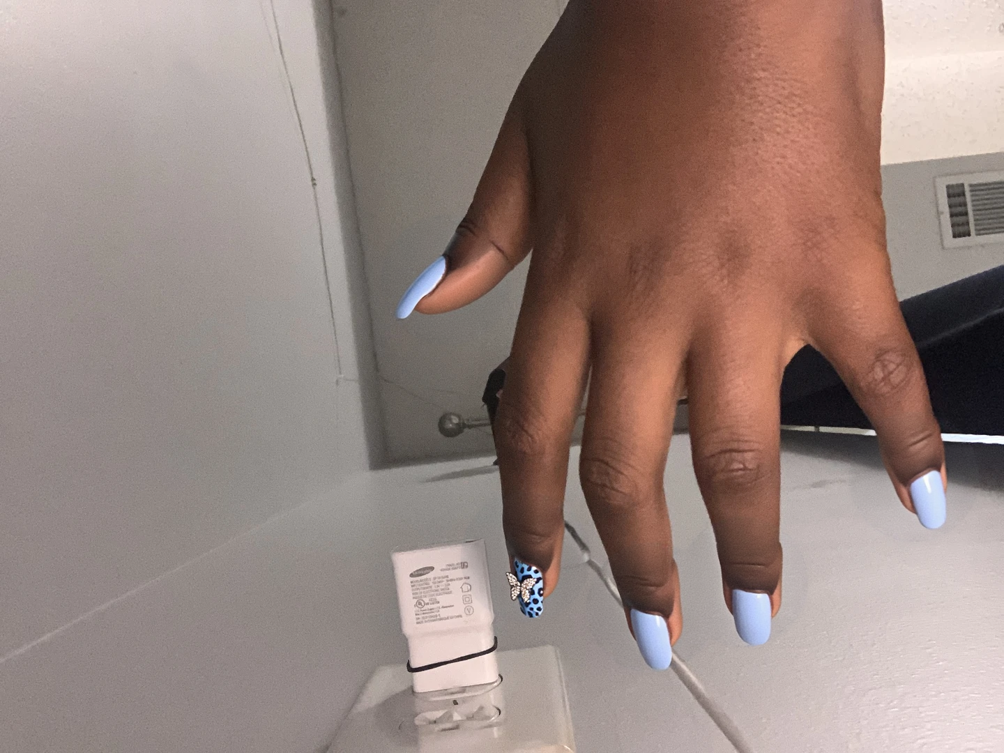 Nails designed with a classic light blue French tip, complemented by a subtle blue cheetah print on the ring finger, adding a playful yet chic element to the overall look. The middle finger features a delicate arrangement of tiny rhinestones, adding a touch of sparkle without overwhelming the minimalist aesthetic. The pinky showcases a charming butterfly charm set against a smooth light blue base, further enhancing the feminine vibe of the design. The remaining nails maintain the elegant light blue base, ensuring a cohesive color scheme that looks polished and trendy, perfectly suited for short square nails.