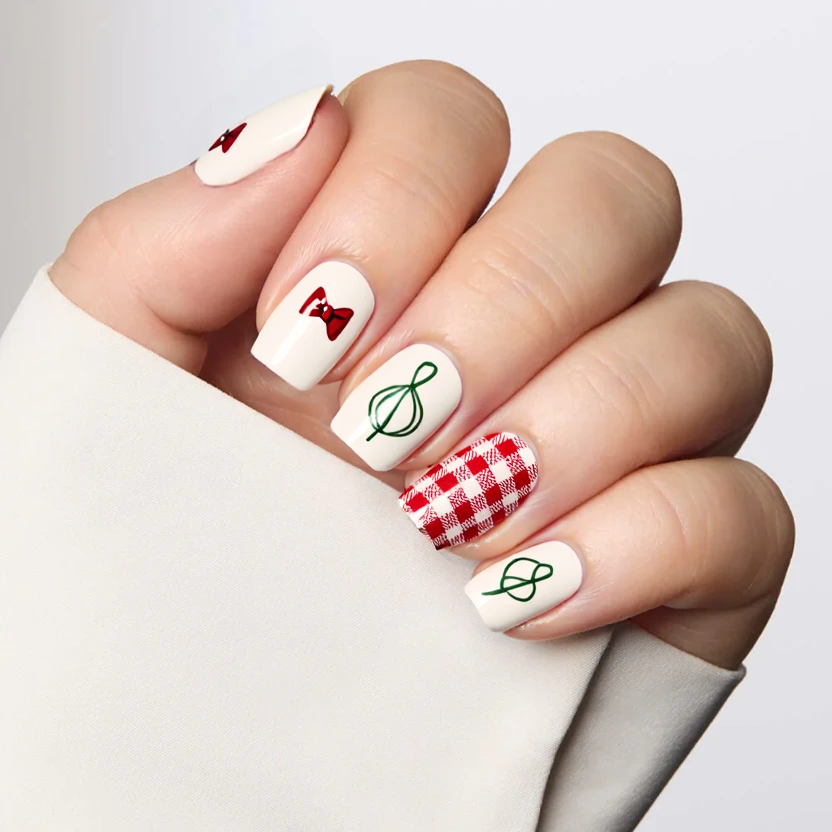 Nails adorned with an elegant take on the classic French tip, featuring a soft ivory base color that elegantly contrasts with a delicate pale pink tip. Each nail showcases a unique yet cohesive design; the index finger displays a minimalist, hand-painted bow in a subtle shade of muted red, harmonizing with the plaid skirt, while the middle finger features a soft plaid pattern in pastel tones of red and white. The ring finger boasts an abstract intertwining line design in an elegant, muted green, reminiscent of holiday wreaths but kept minimalistic for a refined appearance. The pinky finger returns to simplicity with a plain ivory finish. This sophisticated nail art captures the spirit of Christmas without overwhelming the design, perfectly suited for the square shape and short length of the nails.