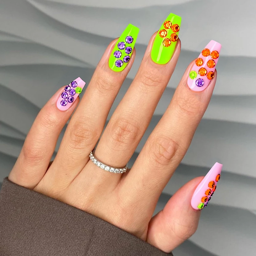 Nails featuring a soft pink jelly base, creating a delicate, translucent appearance that serves as a perfect canvas for the playful Halloween theme. On two accent nails, intricate patterns featuring clusters of 3mm opaque rhinestones in lime green, neon orange, and bright purple are carefully arranged, reminiscent of whimsical candy motifs, with no more than four rhinestones on each accent nail to maintain an elegant balance. The rest of the nails are kept simple with the pink jelly base to emphasize the charm of the design. The almond shape beautifully showcases the flowing patterns, adding a touch of sophistication to the playful Halloween spirit. A glossy finish enhances the overall look, ensuring the set radiates with a fun, feminine flair.