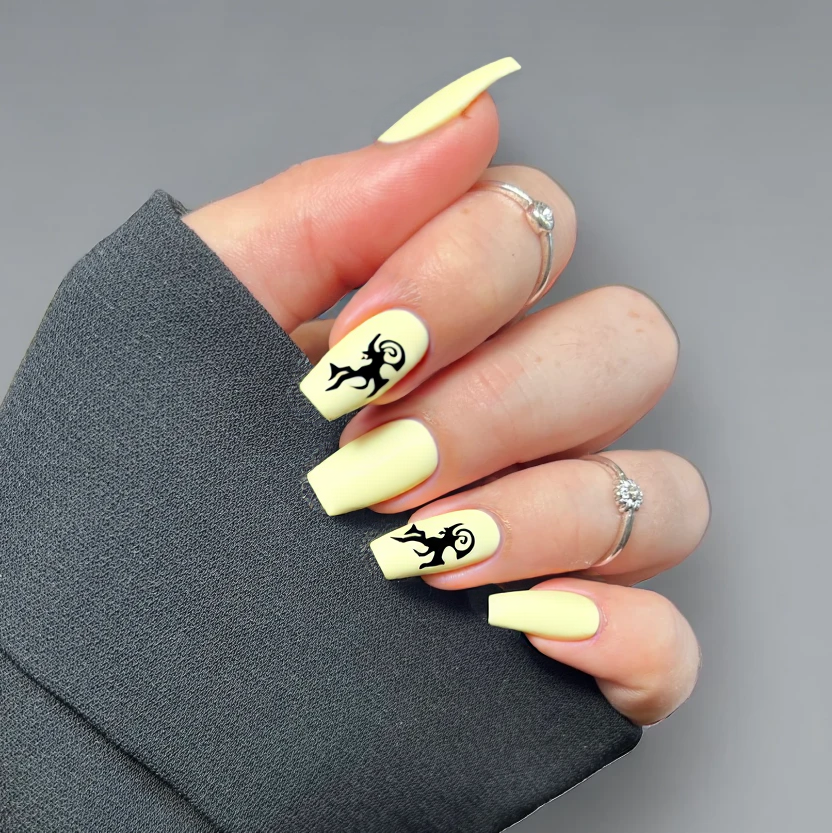 Nails featuring a soft, matte buttercup yellow base color that provides a warm and inviting backdrop. On the ring fingers, a delicate, hand-painted black silhouette of a griffin, gracefully curled with its wings slightly extended, adds an intriguing focal point. The other nails remain plain with the same buttery hue, ensuring an elegant and minimal look. The almond shape enhances the flowing curves of the griffin design, while the overall aesthetic maintains a sophisticated balance of simplicity amidst the artistic detail.