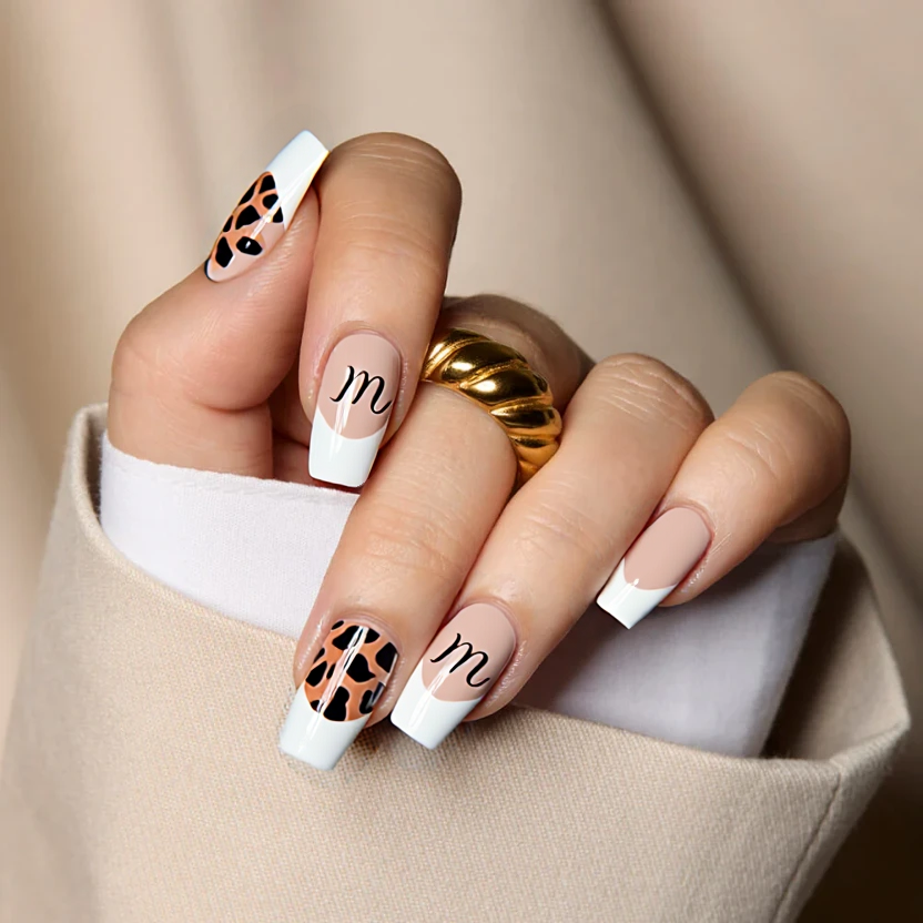 Nails adorned with a classic French tip design featuring a soft nude base color that gracefully transitions to elegant white tips. The playful twist is introduced with delicate, minimalist leopard print patterns, composed of subtle brown and black spots, adorning the ring finger as a chic accent. Additionally, a tiny cursive 'm' is elegantly incorporated in the same hues, positioned within the leopard print for a cohesive look. The remaining nails showcase the understated beauty of the nude base for a balanced and sophisticated finish, with a glossy top coat that enhances the overall elegance, perfectly complementing the square shape and medium size of the nails.