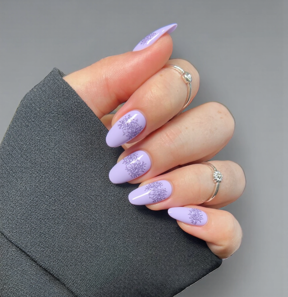 Nails adorned in soft pastel shades of lavender and pale pink, embodying the spirit of Thadingyut, a celebration of lights. A delicate gradient blends these two colors seamlessly from base to tip, creating a calming and ethereal effect. On two accent nails, intricate, hand-painted traditional Myanmar motifs, such as stylized flowers and lanterns, are subtly placed to honor the festive theme, executed in a slightly deeper shade of purple for a touch of elegance. The remaining nails maintain the simple gradient base. A glossy finish enhances the soft colors, perfectly complementing the gentle, flowing lines of short almond-shaped nails.