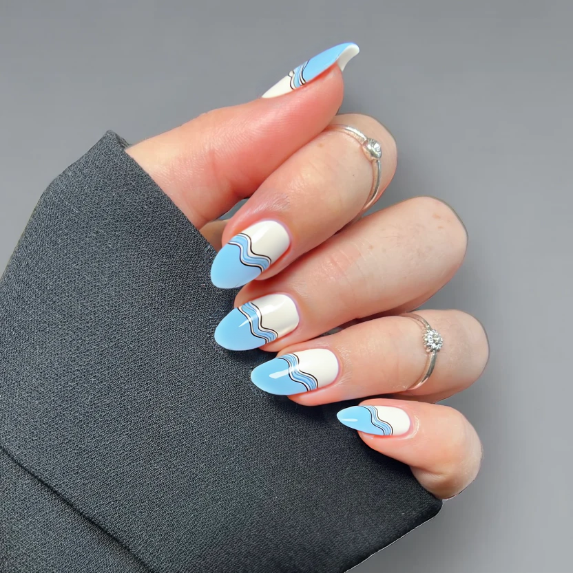 Nails elegantly adorned with a soft, pastel blue base color that evokes the serene beauty of the ocean. The tips are painted in a classic French manicure style, delicately transitioning to a clean white, capturing the essence of sandy shores. To enhance the aquatic theme, minimalistic wave patterns in a lighter shade of blue gently ripple across the ring fingers, while the remaining nails maintain their polished simplicity. A glossy finish adds a sophisticated shine, perfectly complementing the graceful almond shape of the short nails, creating a chic and formal beach-inspired look.