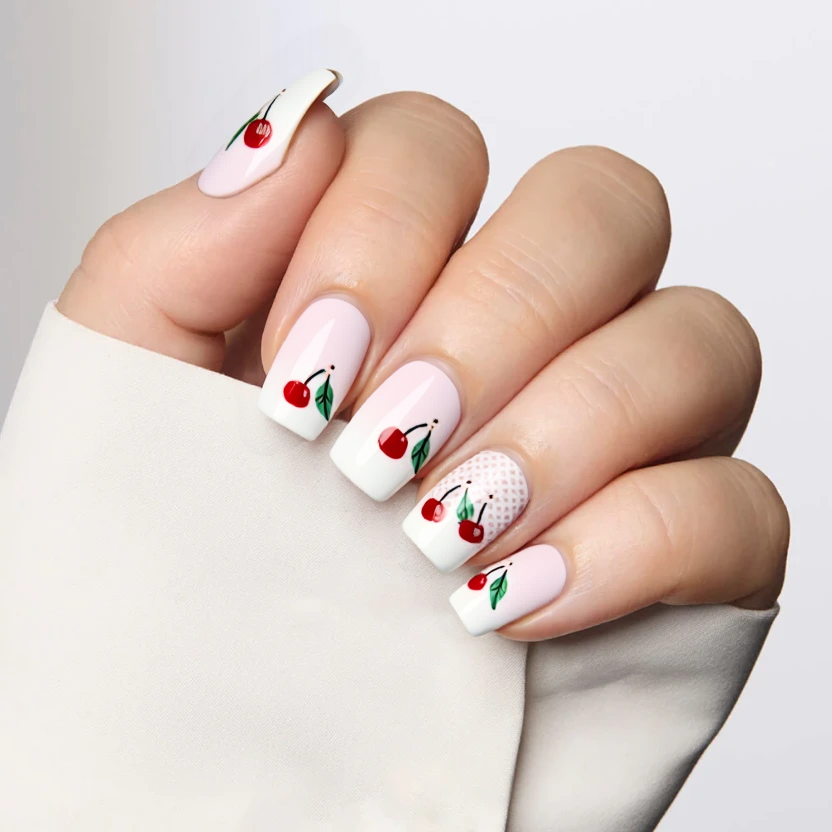 Nails elegantly adorned with a classic white French tip design on a soft pastel pink base, showcasing a delicate lace pattern at the cuticle area of the nails. On the ring fingers, a minimalist arrangement of hand-painted cherry motifs consisting of two cherries with green leaves is gracefully placed at the center, adding a subtle pop of color. The remaining nails feature the French tip and lace pattern only, creating a beautifully harmonious look. The overall finish is glossy, enhancing the feminine charm of these medium almond-shaped nails.